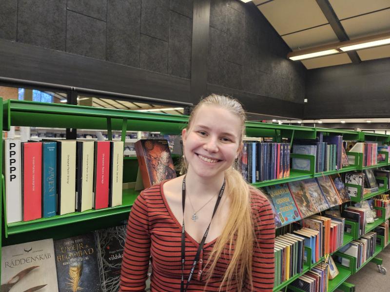 Portræt af Anne Asaa med bibliotek i baggrunden. Hun er tovholder for læseklubben ”Læsepiloterne” på Odder Bibliotek