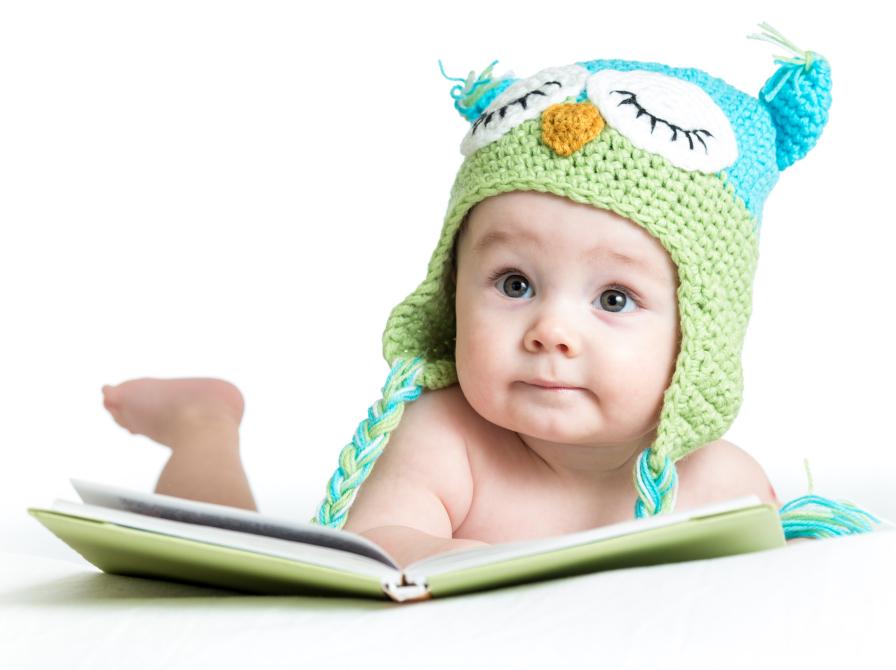 Baby med hue kigger i en billedbog.
